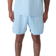 A person wears true to size POTENTIAL SWEATSHORTS BLUE with BNDT lettering on the left leg and a matching blue shirt, standing with arms relaxed at their sides against a white background.
