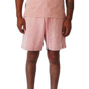 A person wears mauve POTENTIAL SWEATSHORTS made of heavy GSM cotton with BND embroidery on the left leg, paired with a light pink T-shirt, standing relaxed against a white background.