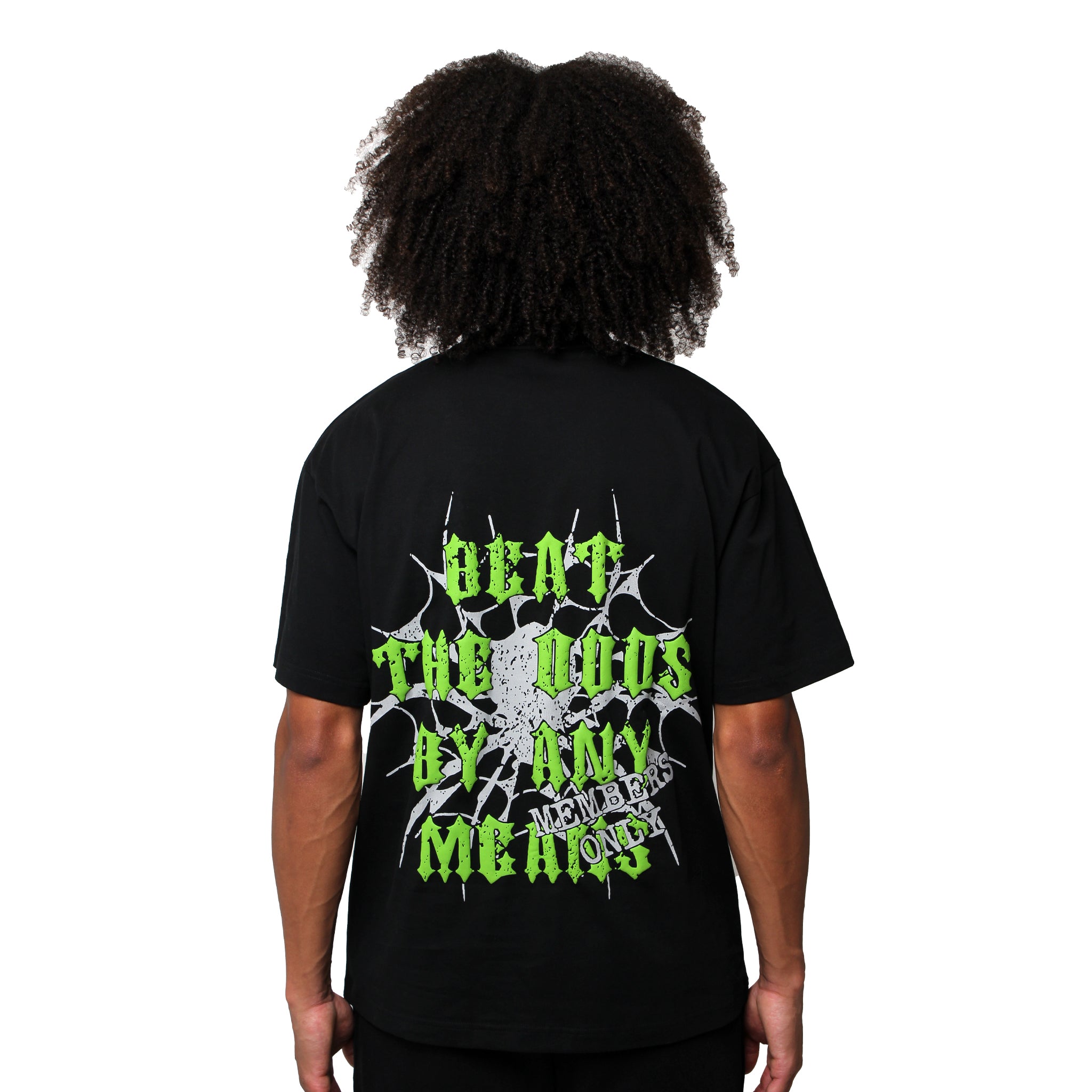 A person with curly hair, facing away from the camera, is wearing the BEAT THE ODDS S/S TEE BLACK, featuring neon green and white graphic text on the back that reads "Beat the Odds by Any Means Necessary.