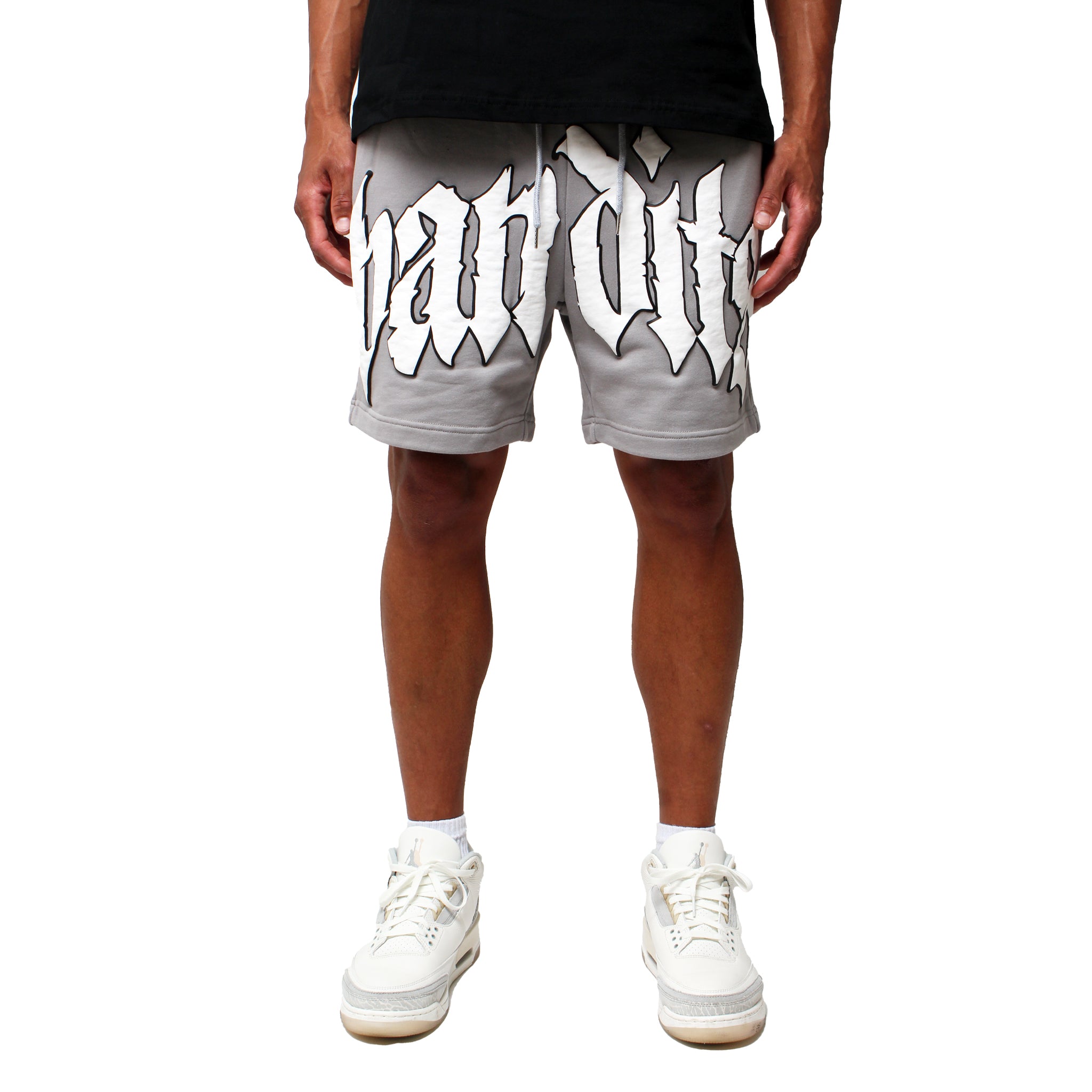 Wearing EGO SWEATSHORT GREY with bold white 3D Puff Print gothic lettering, paired with white sneakers; the visible shot shows only legs and lower torso against a plain white background.