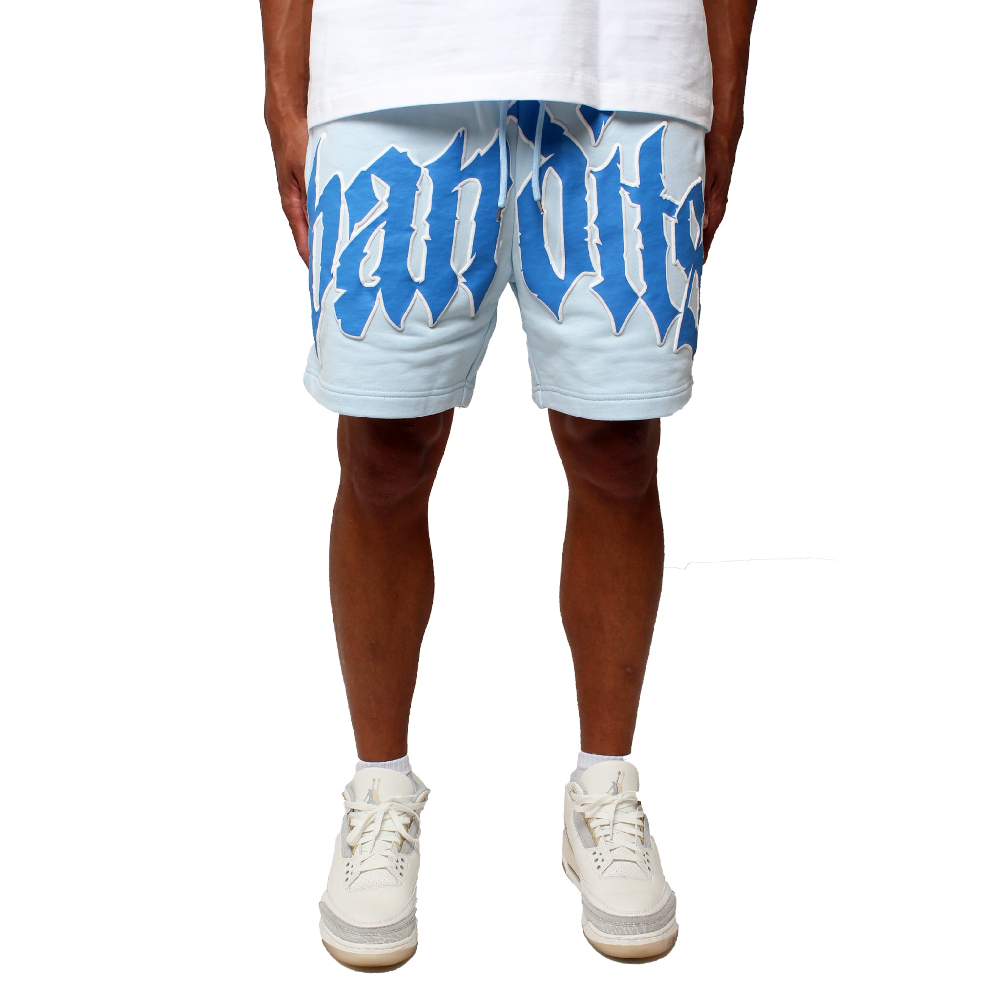Wearing EGO SWEATSHORT LT. BLUE with large 3D Puff Print text, a white T-shirt, and white high-top sneakers, the person stands against a plain white background; only the lower body is visible.