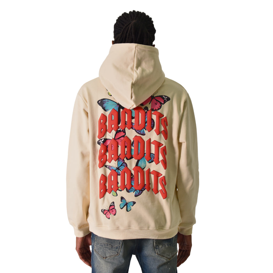 Wearing the FLY FREE PULLOVER HOODY TAN featuring bold red gothic "BANDITS" lettering and colorful butterfly graphics on the back, paired with blue jeans for a standout streetwear look.