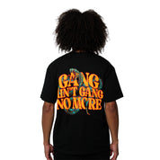 Person with curly hair wears the GANG AIN'T GANG NO MORE S/S TEE BLACK, an oversized heavy cotton T-shirt featuring bold orange and yellow back text “GANG AIN’T GANG NO MORE” with a snake graphic winding through the letters.