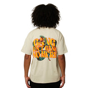 Seen from the back, a person with curly hair wears the GANG AIN'T GANG NO MORE S/S TEE TAN, featuring colorful puff printed text and a bold snake graphic.