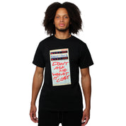 A person with curly hair wears the GUEST CHECK S/S TEE BLACK, a vintage-style black cotton shirt featuring a guest check receipt and bold red text, “DON’T ASK ME WHAT IT COST,” shown on a plain white background.