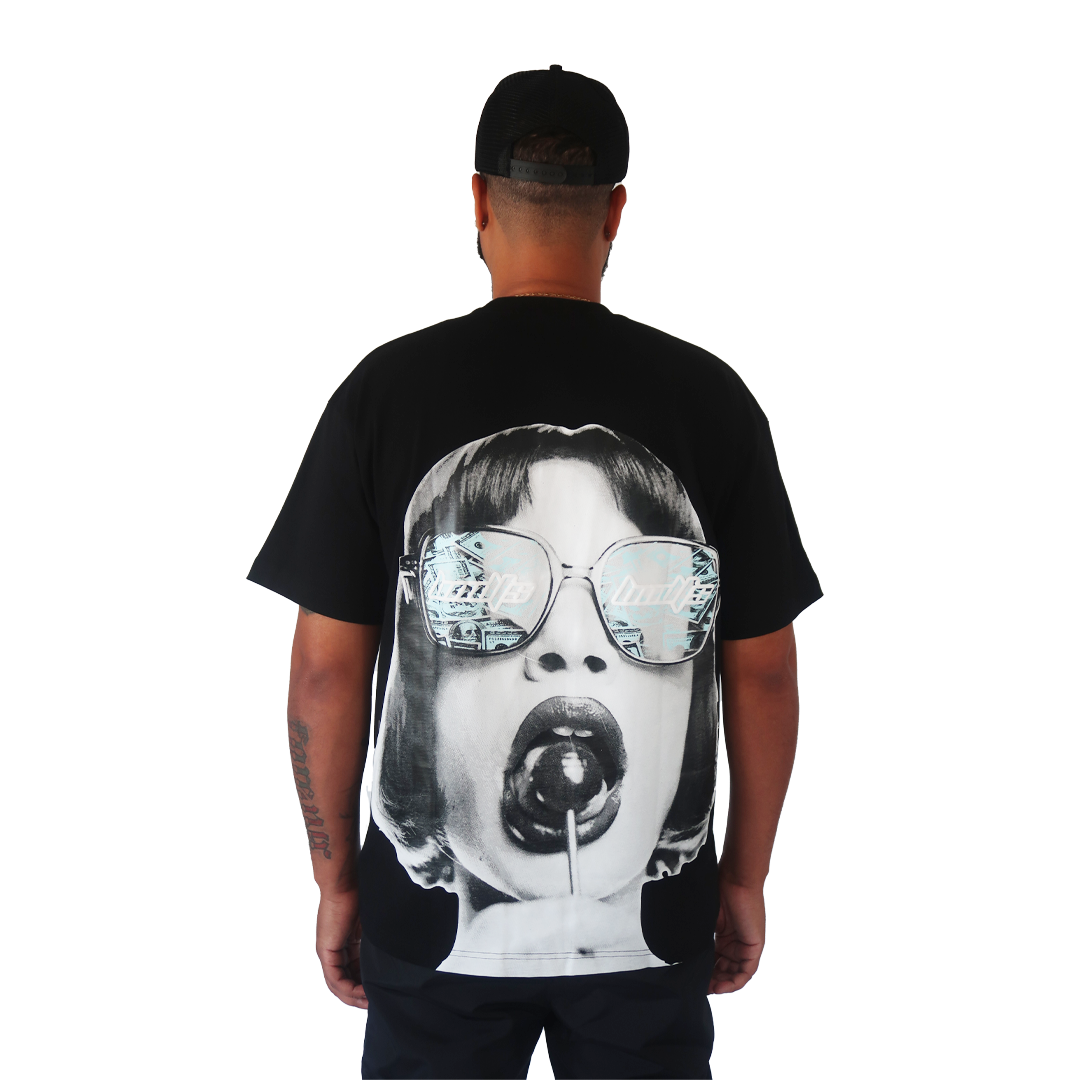 S TEE BLACK stands facing away. The oversized tee features a large retro graphic of a bob-haired woman with sunglasses and a lollipop on a plain white background.