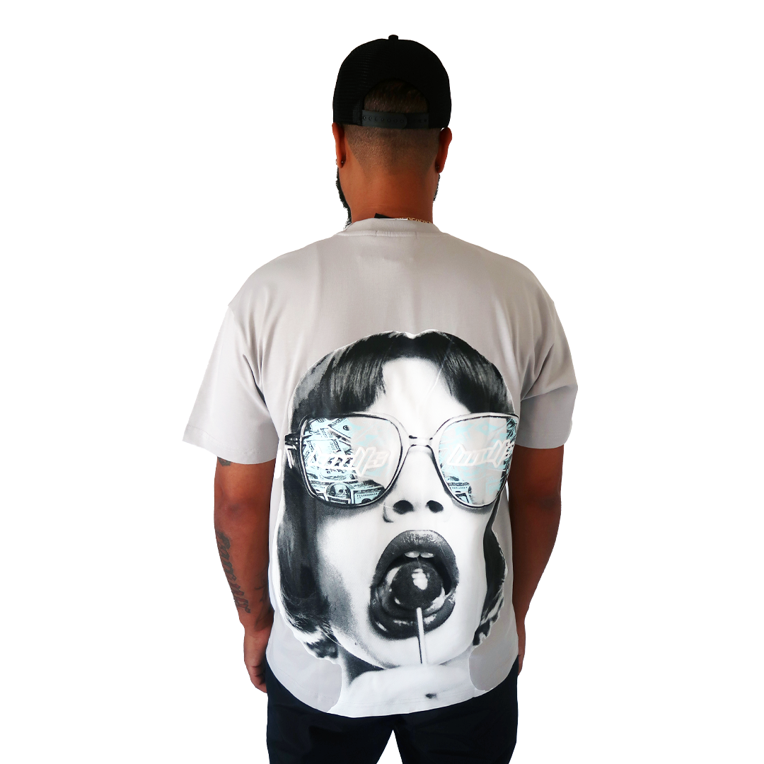 S TEE GREY, an oversized streetwear shirt with a retro woman and lollipop back graphic, paired with a black cap as he stands facing away from the camera.