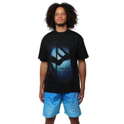 Someone with curly hair wears the MAIN STAGE S/S TEE BLACK and blue shorts, standing against a plain white background.