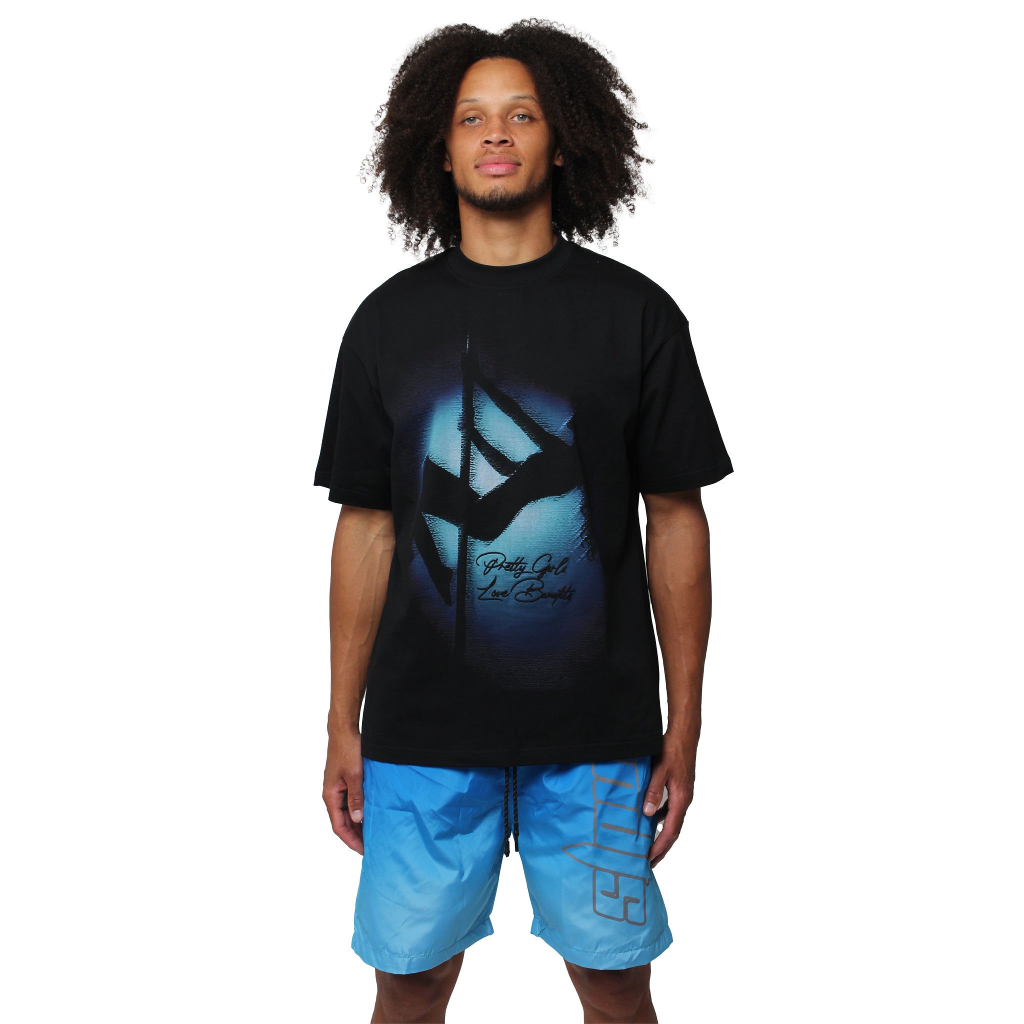 Someone with curly hair wears the MAIN STAGE S/S TEE BLACK and blue shorts, standing against a plain white background.