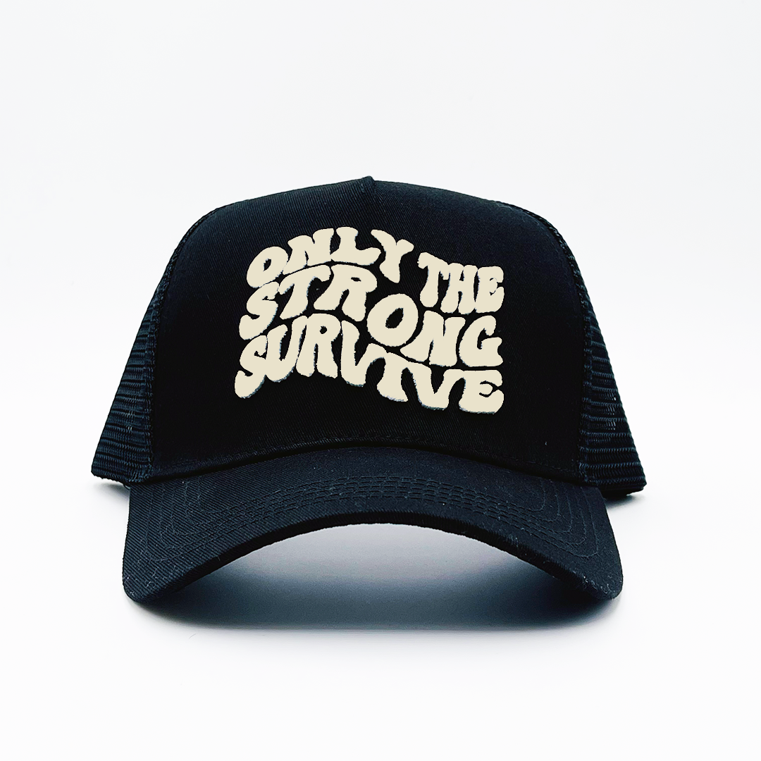 The ONLY THE STRONG SURVIVE TRUCKER is a black hat featuring bold, wavy white 3D embroidered text on the front and an adjustable snapback for a perfect fit. Shown against a plain white background.