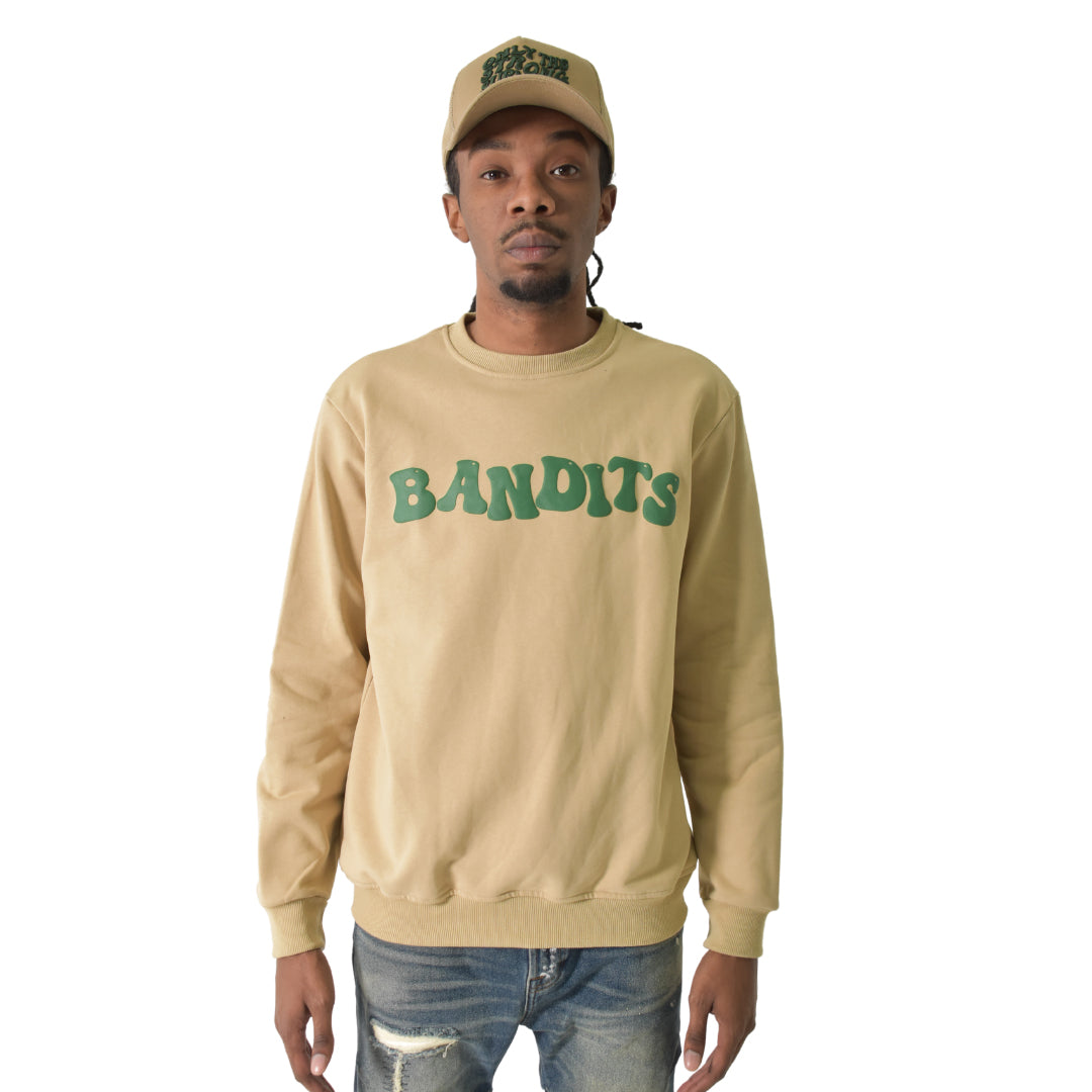 A man in the ONLY THE STRONG SURVIVE CREWNECK SWEATSHIRT TAN with a 3D Puff Print "BANDITS" graphic and matching cap stands facing forward in ripped blue jeans. The heavyweight French terry fleece blends comfort and style against a white background.