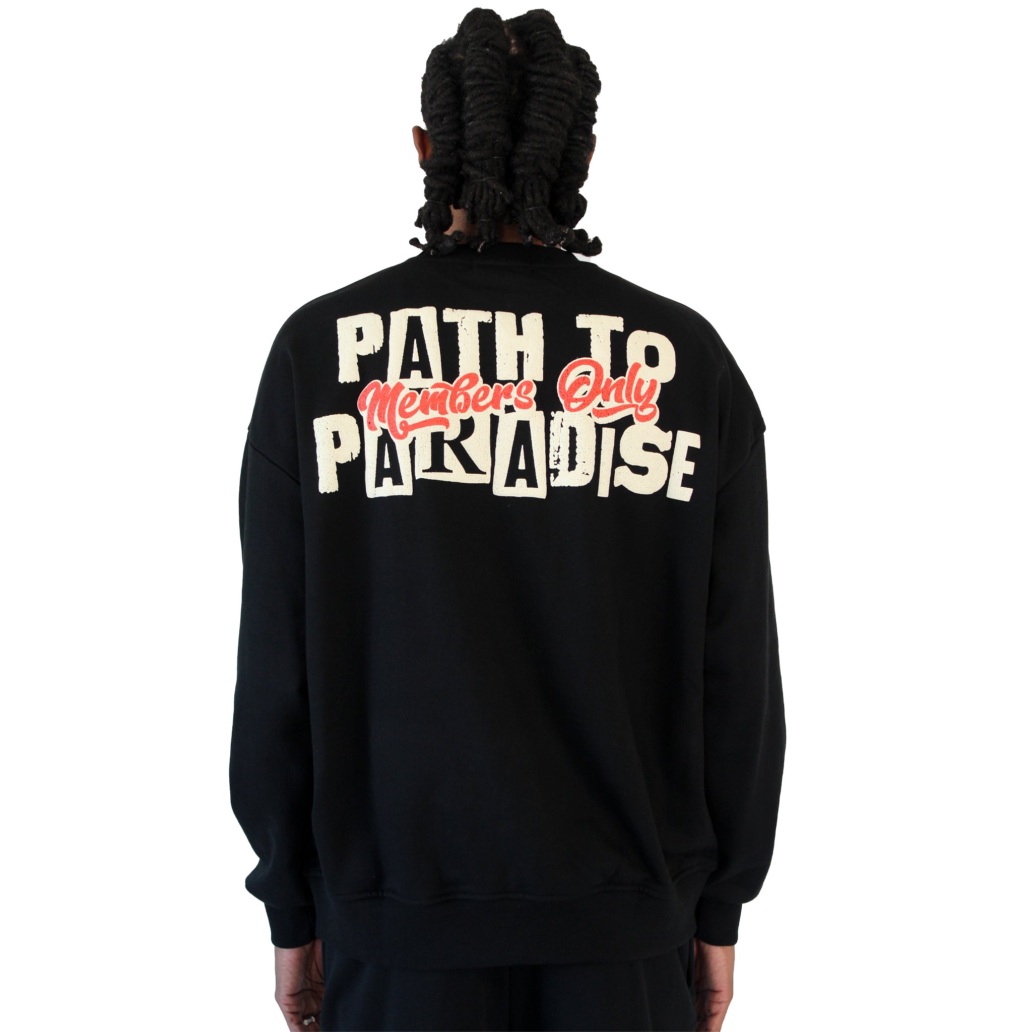 A person with long, twisted hair is seen from the back wearing the PATH TO PARADISE CREWNECK SWEATSHIRT BLACK, featuring bold white "PATH TO PARADISE" text and "Members Only" in red cursive on the back, channeling modern streetwear style.