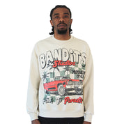 A man with braided hair sports a modern streetwear vibe in the PATH TO PARADISE CREWNECK SWEATSHIRT TAN, showcasing colorful graphics of a red vintage lowrider, palm trees, and bold BANDITS Studios Members Only Palm to Paradise text on white.