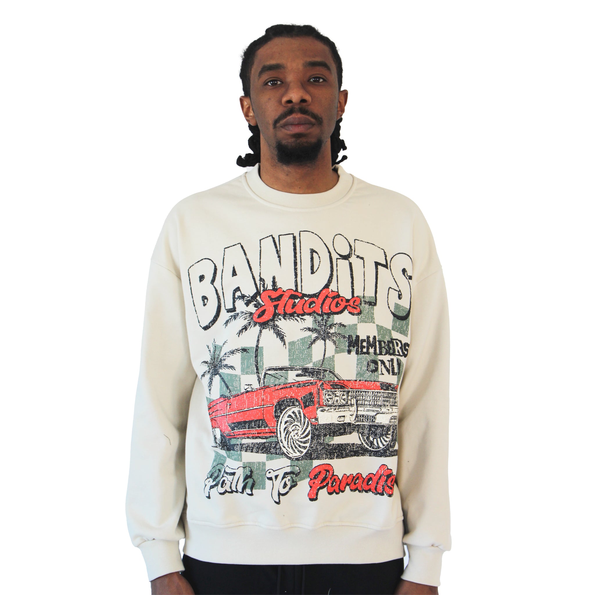 A man with braided hair sports a modern streetwear vibe in the PATH TO PARADISE CREWNECK SWEATSHIRT TAN, showcasing colorful graphics of a red vintage lowrider, palm trees, and bold BANDITS Studios Members Only Palm to Paradise text on white.