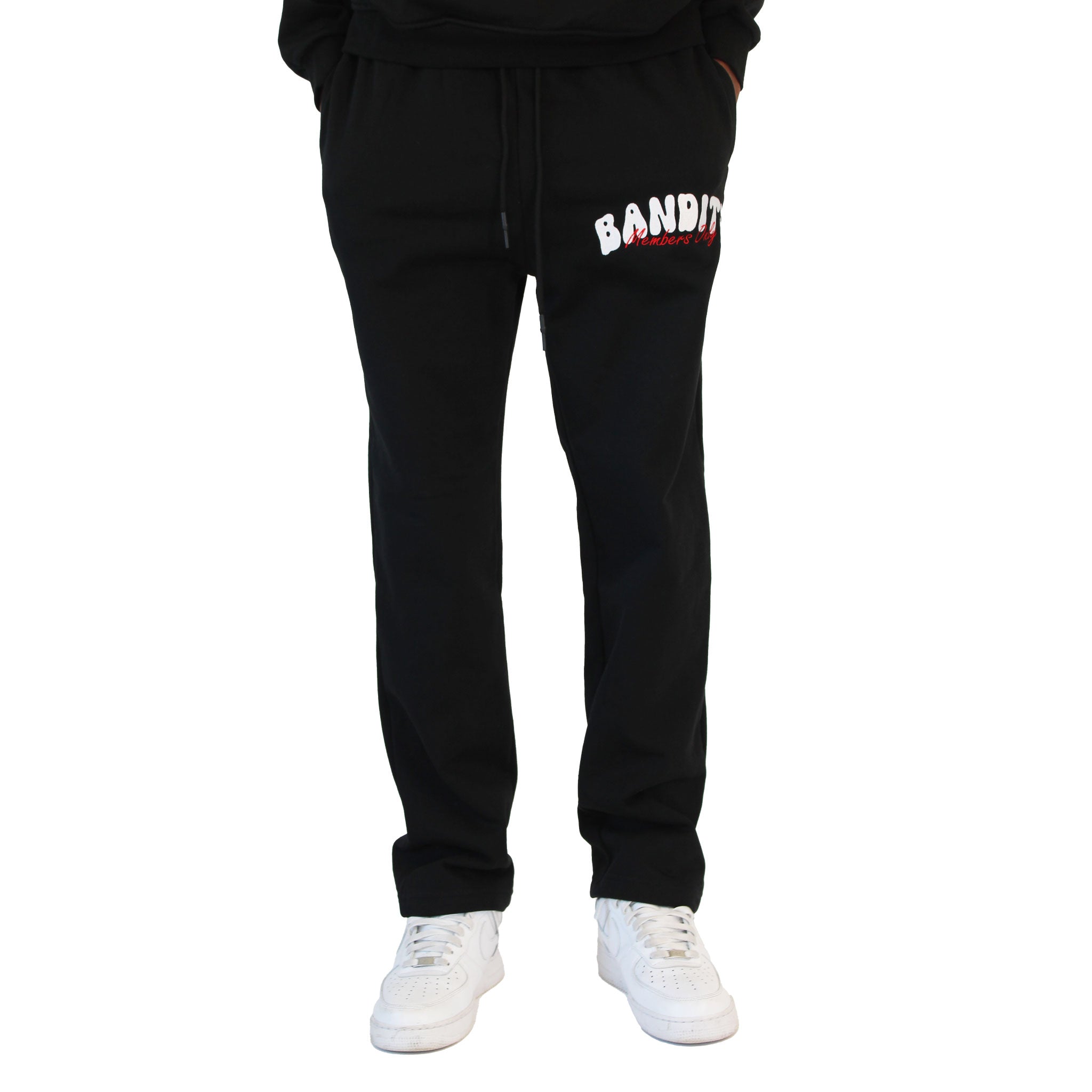A person sports BIKER CLUB SWEATPANTS BLACK with "BANDIT" in white and red on the left thigh, teamed with white sneakers. The bold streetwear fleece pants stand out, while the upper body is not visible.