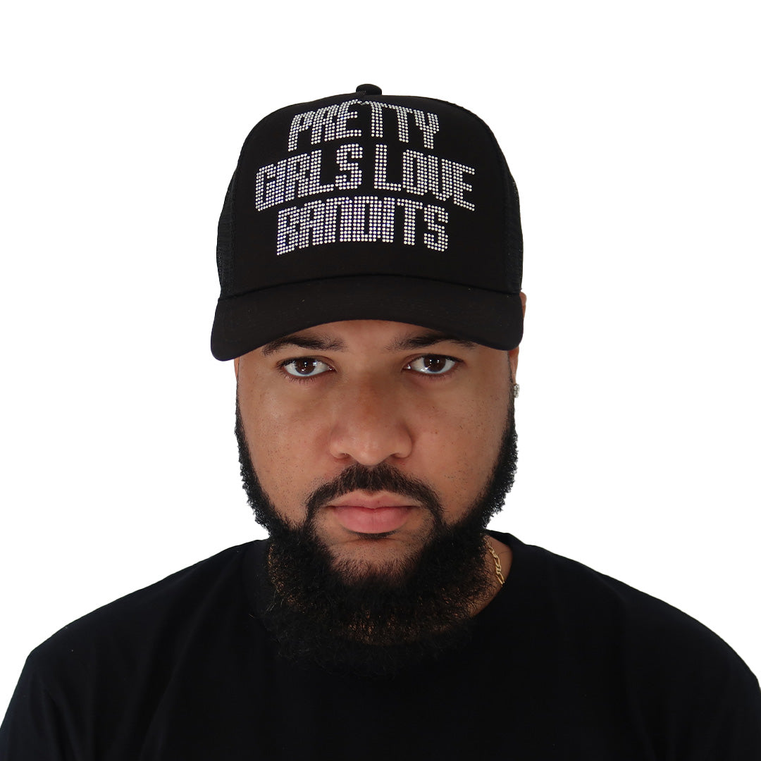 A bearded man wears the PGLB RHINESTONE TRUCKER hat—black with "PRETTY GIRLS LOVE DIAMONDS" in white capitals—and a matching T-shirt. The adjustable snapback fits snugly on his head against a plain white background.