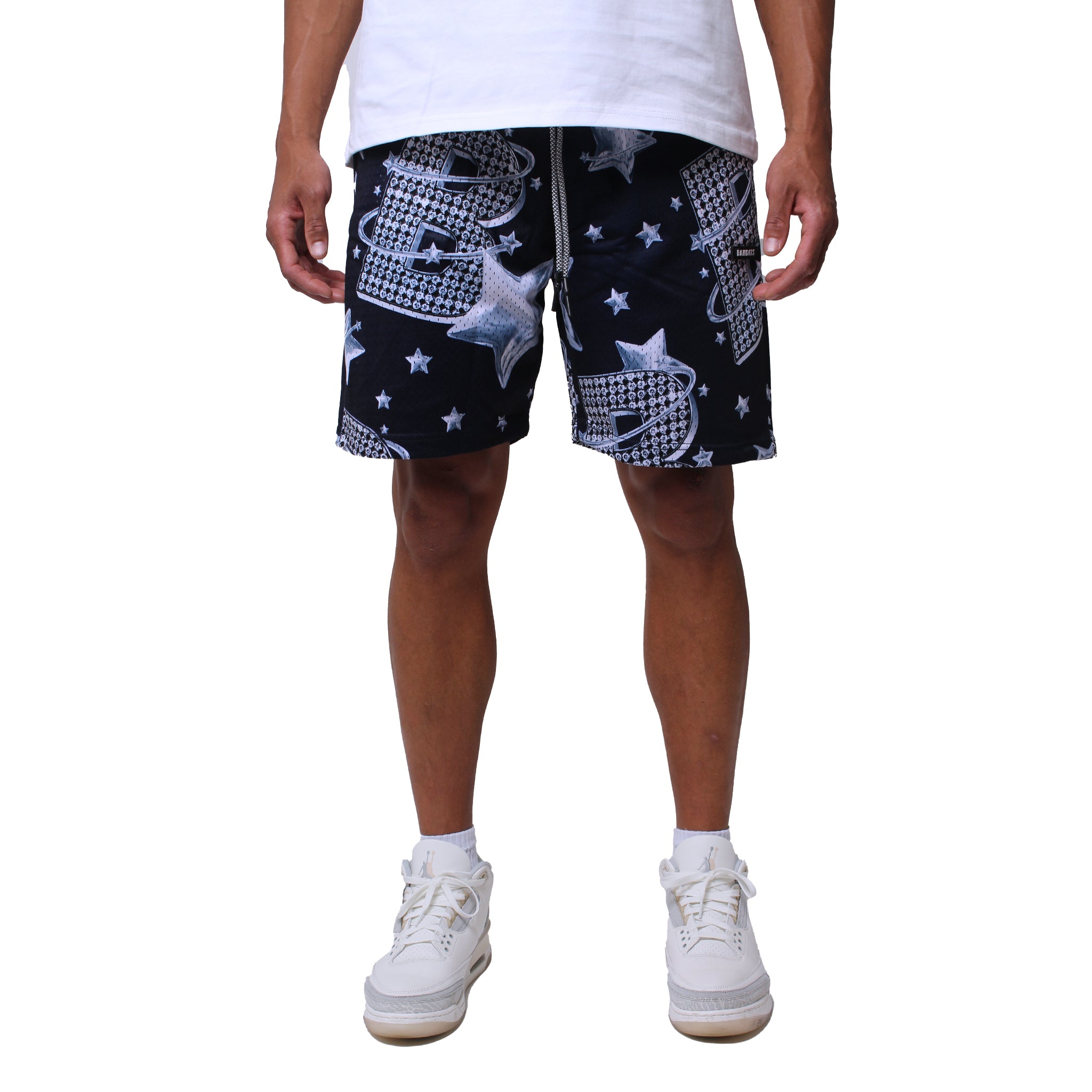 A person stands against a plain white background wearing a white T-shirt, VVS MESH SHORTS NAVY with white star and graphic designs, and white sneakers, arms relaxed by their sides.